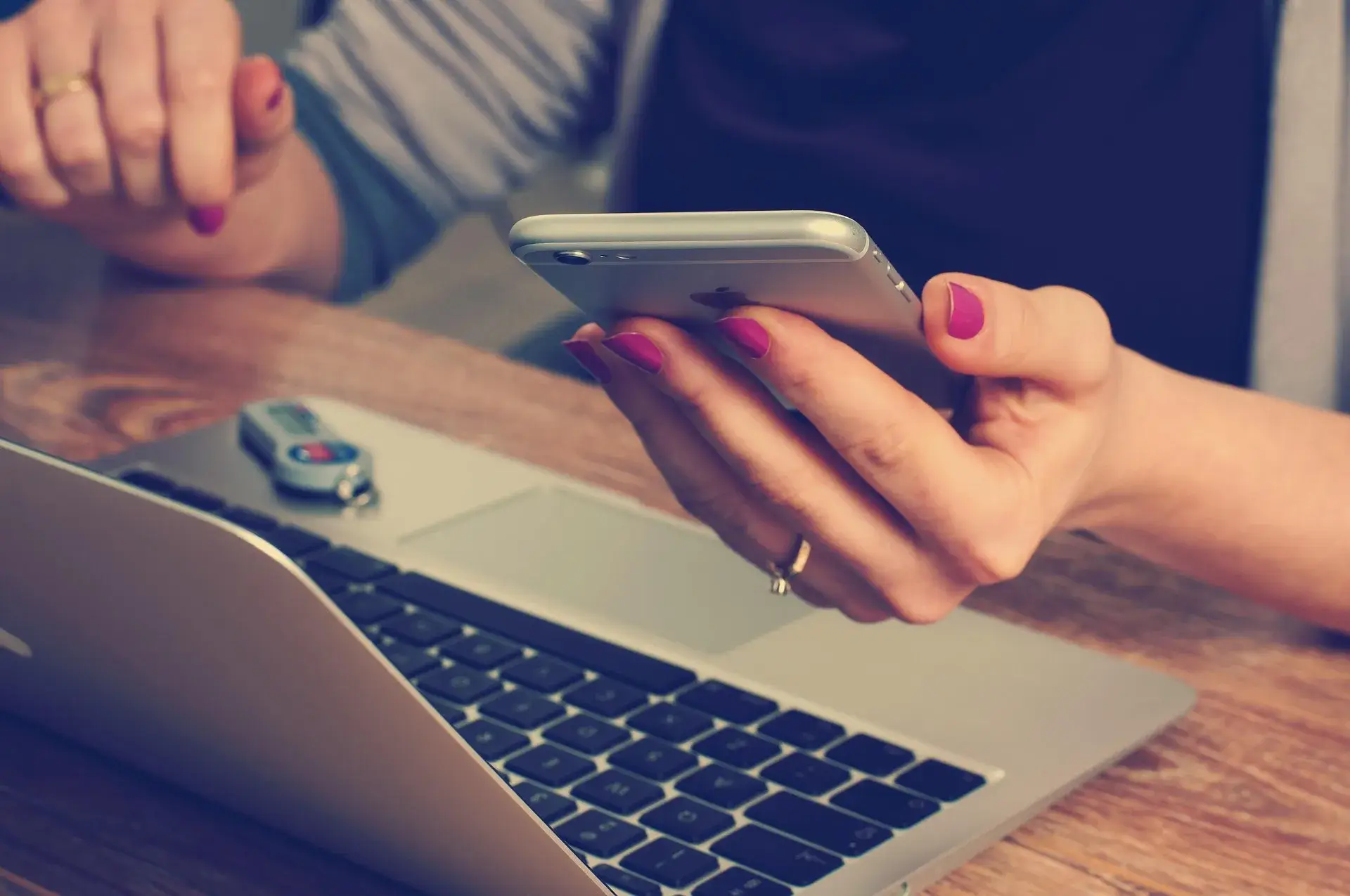 Close up of woman's hands as she holds a phone and works on a laptop.